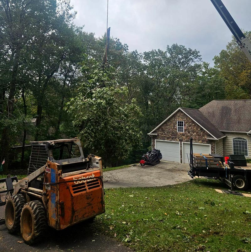 Next Generation Tree Service working a residential tree removal job featuring a skid steer and crane lifting a tree.